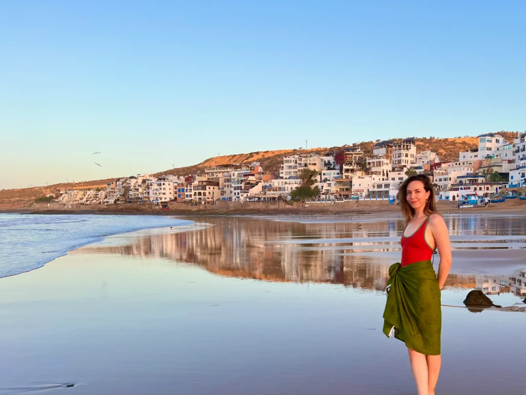 Girl standing on Taghazout beach when the pink hues of the sun rising over the town.